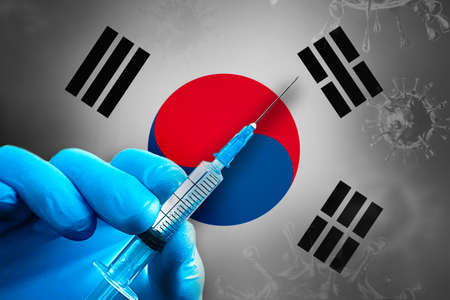 South Korea Covid-19 Vaccination Campaign. A hand in a blue rubber glove holds a syringe with covid-19 virus vaccine in front of South Korea flag. Coronavirus vaccination conceptの写真素材