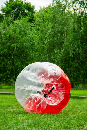 Red Zorbing Balloon on the summer lawn. Inflatable zorb ball outdoor. Leisure activity concept with...