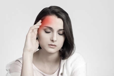 Tired sad brunette woman touches her head, migraine, pain area of red color. Headache conceptの写真素材