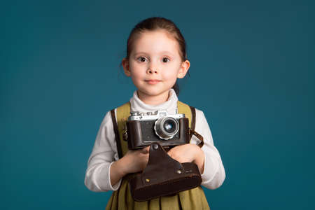 Cute little smiling girl photographer with old camera. Studio portrait on blue background.の写真素材