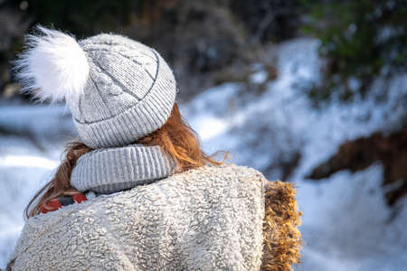 Rear view on blond young woman in winter clothes and beanie hat outdoor.の写真素材