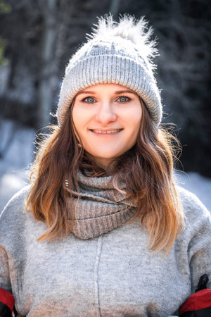Winter vertical portrait of caucasian blond young smiling happy woman in gray sweater and beanie hat outdoor.の写真素材
