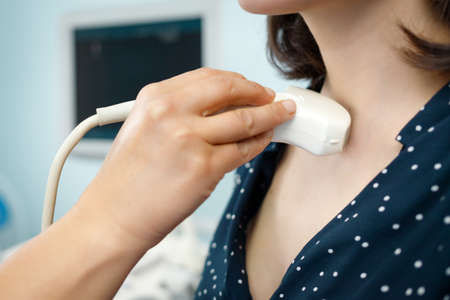 Diagnostic examining patient woman thyroid gland using ultrasound scanner machine, close-up hands.の写真素材