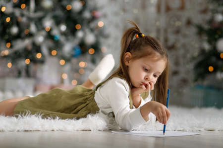 Cute little girl 5 years old pensively draws lying on the floor in christmas interior.の写真素材