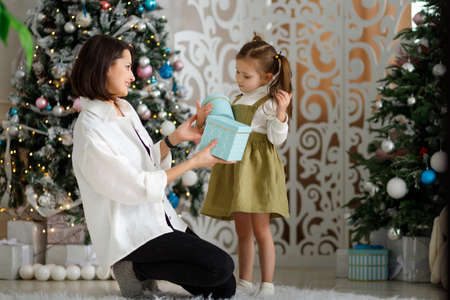 Pretty kid girl with her young mother give each other new year gifts in cozy christmas interior.の写真素材