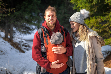 Babywearing winter forest walk with family and their baby son in ergonomic carrier.の写真素材