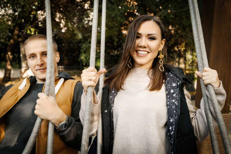Young mixed race couple smiling happy on swing, Asian woman, Caucasian man outdoor.の写真素材