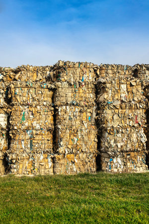 Large stacks of waste paper for recycling on the grass outdoors, vertical copy space.