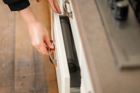 Close-up on woman's hands taking out kitchen utensils from kitchen drawer for cooking homemade food. Selective soft focus, copy space.の写真素材
