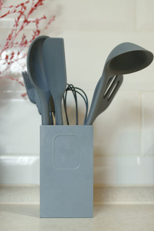 Silicone kitchenware such as ladles, spatulas and whisk in a stand on a home kitchen table.