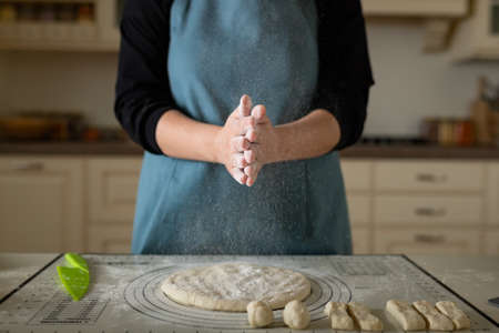 Clapping hands in flour of a cook in a blue apron in a home kitchen.の写真素材