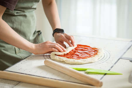 A woman in a green apron cooking a sweet roll with jam on a white silicone cooking mat.の写真素材