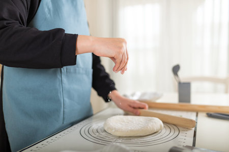 Chef in apron sprinkles flour on cooked wheat pastry dough on silicone baking mat. Selective focus,...