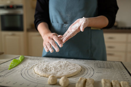 Hands in flour at the cook in a blue apron in a home bakery.