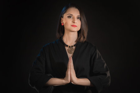 Woman look at camera with zen hands or praying hand symbol on a black background.