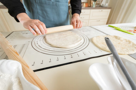 A woman rolls out dough on a silicone baking mat with markings.
