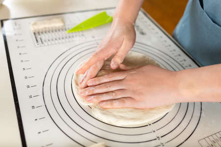 Close-up on female hands crumpling fresh kneaded dough on a kitchen baking mat.の写真素材
