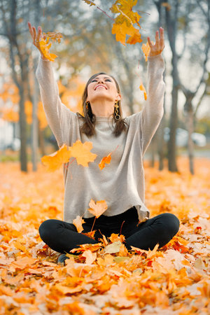 Happy mixed race young woman smiling joyful throws up autumn leaves outside in fall forest, copy...