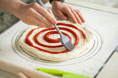 Applying berry jam to dessert roll dough with a kitchen brush.