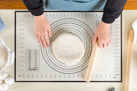Top view of cooked wheat dough and hands of chef with rolling pin in hand on kitchen work surface.の写真素材