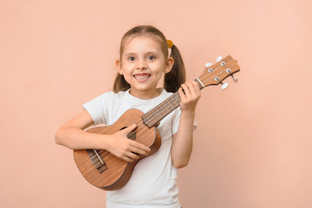 Happy funny caucasian smiling girl 6 - 8 years old in a white t-shirt with a ukulele on a pink background.の写真素材