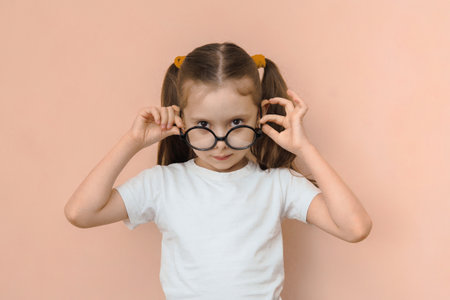 Portrait of a funny kid girl of elementary school age in round optical glasses on a pink background.の写真素材