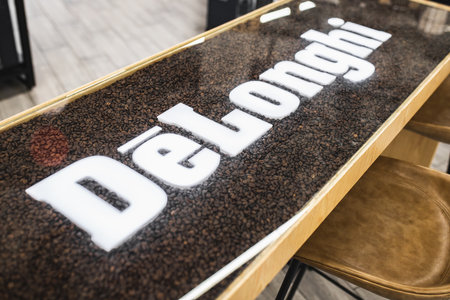 DeLonghi logo on a table with real coffee beans under glass in a coffee shop. Almaty, Kazakhstan - April 16, 2023のeditorial素材