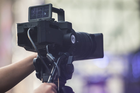 Operator with a video camera records a reporting event at an open public event, close-up.
