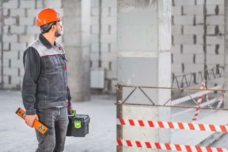 A foreman inspects a new apartment before starting work. Builder in uniform carrying toolbox and...