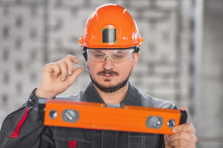 Construction worker portrait with level tool, caucasian bearded man in hard hat, protective glasses...