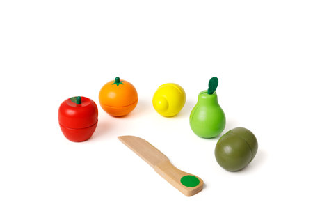Multi-colored toys in the shape of fruits and a wooden knife for cutting these fruits. Educational games for younger preschoolers. Copy space and white background.の写真素材