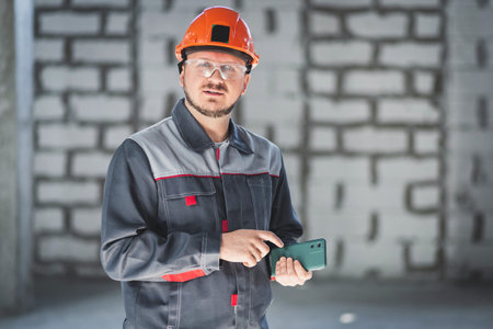 Caucasian construction worker in overalls and helmet uses a smartphone with cameras in his professional work.の写真素材