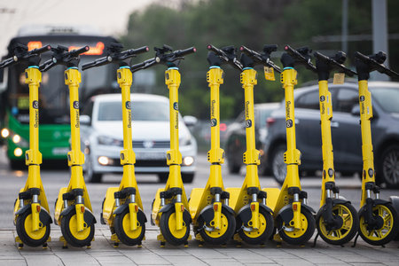 Many electric scooters from Yandex, ready for rent, stand on the sidewalk against the backdrop of a...