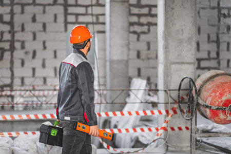 Construction worker with a suitcase with tools and level tool, in overalls, walks along a...