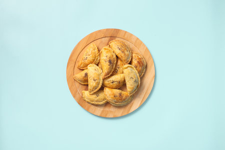 Top view baked samsa pies with chicken sprinkled with poppy seeds on wooden plate on blue background.の写真素材