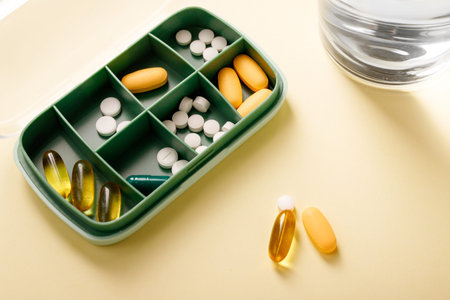 Pill box with various pills, vitamins and dietary supplement next to water glass and omega 3...