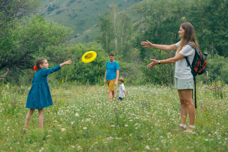 Children enjoy outdoor play, tossing a frisbee in a vibrant green field with mountains in the background.の写真素材