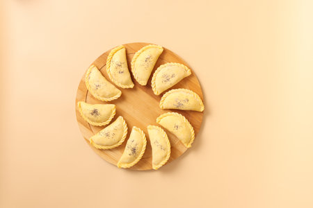 Top view on raw samsa with meat and poppy seeds on a wooden round board ready for baking. Traditional Central Asian cuisine bakery, frozen semi-finished products, copy space.の写真素材