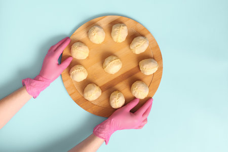 Flat lay shot of Central Asian manty arranged on a circular wooden board, with cook hands in rubber gloves.の写真素材