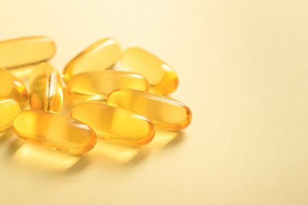 Close up of handful golden color oil fish fat omega-3 in soft gel capsule on yellow background, copy space.の写真素材