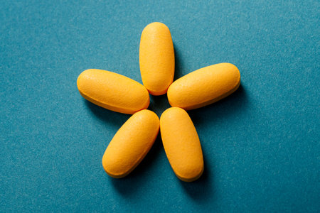 Close up of 5 yellow pills or Dietary supplement laid out in the shape of a star on blue background.の写真素材