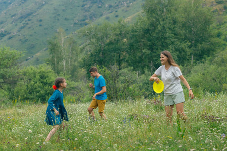 Children and an adult joyfully play frisbee in a vibrant meadow with stunning mountains in the backgroundの写真素材