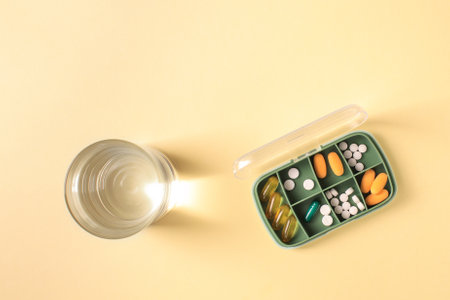 Pill box with various pills and vitamins and a glass of water, top view, copy space.の写真素材