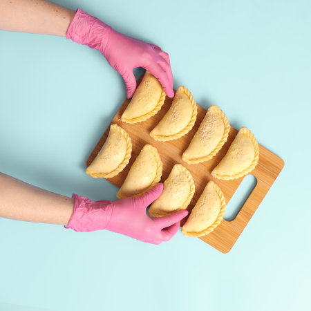 Flat lay a woman bakers hands in a pink rubber gloves lays out raw pies on blue background, frozen semi-finished products.の写真素材