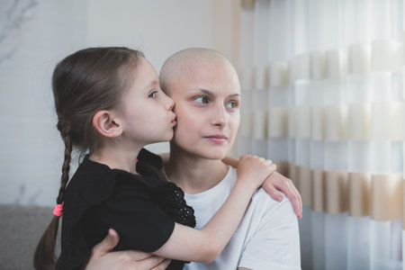 Caring kid girl hugs and kiss her mother with a diagnosis of oncology indoor. Family support concept.の写真素材