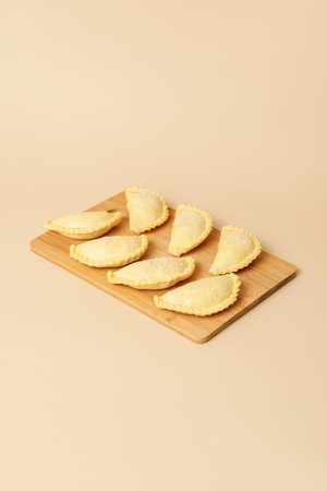 Raw samosas with sesame on a wooden brown board. Traditional food, frozen semi-finished products,...