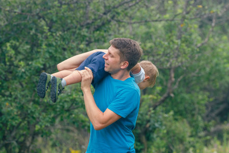 A joyful father enjoys a fun moment outdoors with his child in a lush natural environment, making memoriesの写真素材