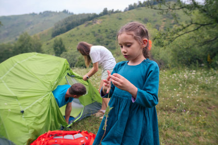 A cheerful family sets up a tent while a child explores nature, capturing the essence of outdoor adventureの写真素材