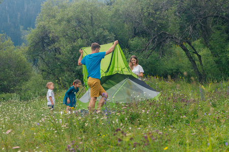A joyful family happily sets up a colorful tent in a beautiful, lush meadow that is surrounded by treesの写真素材