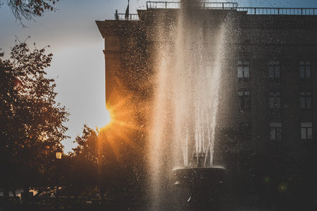 Close-up of fountain water droplets sparkling against the setting sun and a historic building...
